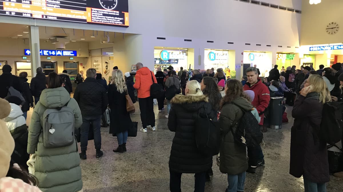 Tampereen rautatieaseman aulahalli täynnä ihmisiä tutkimassa aikataulunäyttöä.