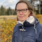 Kyläasiamies Elina Leppänen katsoo hymyillen kameraan sininen takki yllään. Taustalla ruskan värjäämiä pensaita.Tuuloksessa 4.10.2021.
