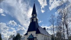 Rovaniemen kirkko kesäpäivänä, aurinko paistaa kirkontornin takaa