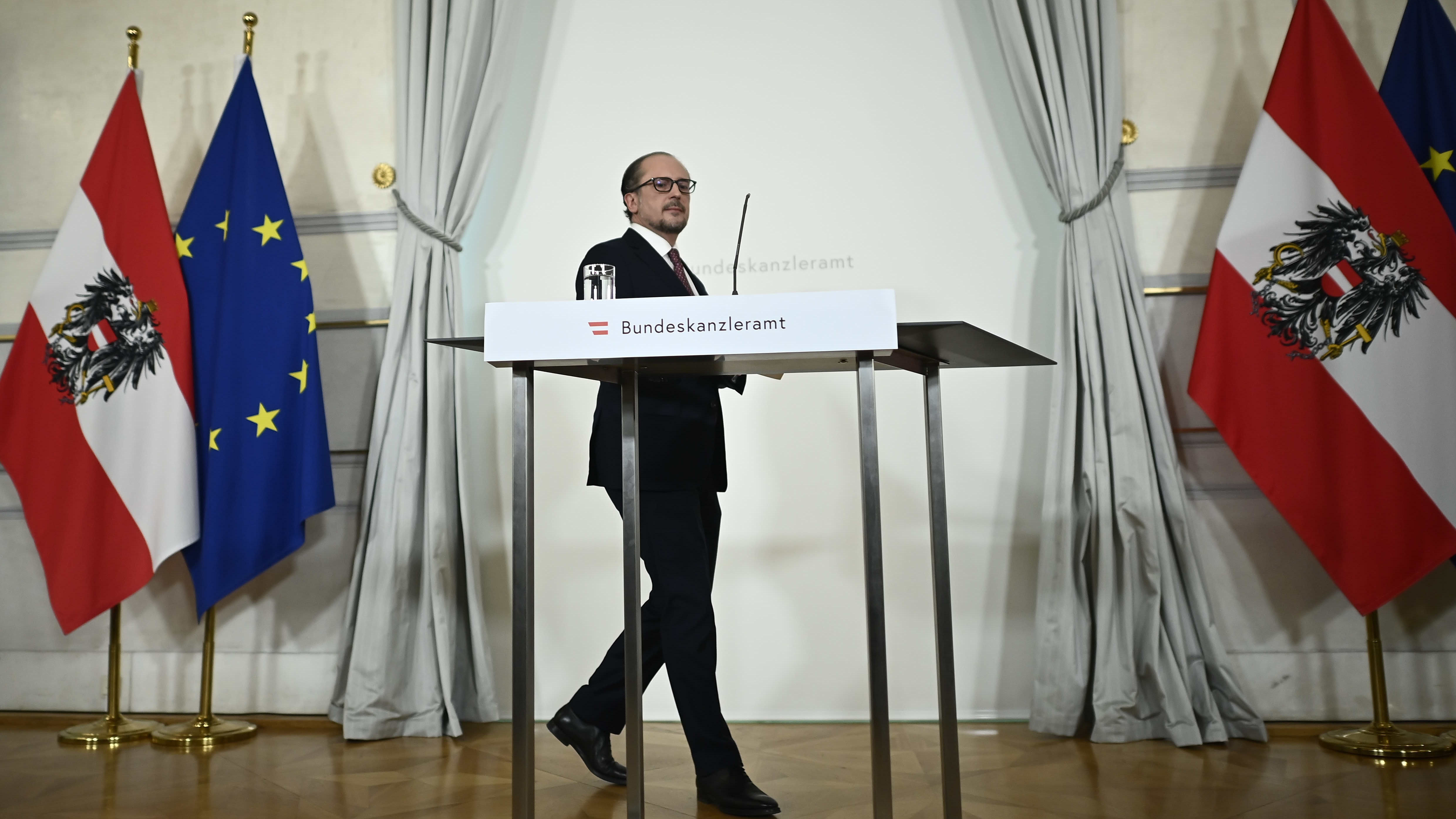 Mies kävelee puhujapaikalle, taustalla Itävallan ja EU:n liput