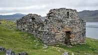 Ruinerna av en gammal gråstenskyrka på Grönland, med en fjord i bakgrunden.