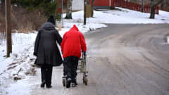 Kaksi henkilöä kävelee tiellä, toisella rollaattori.