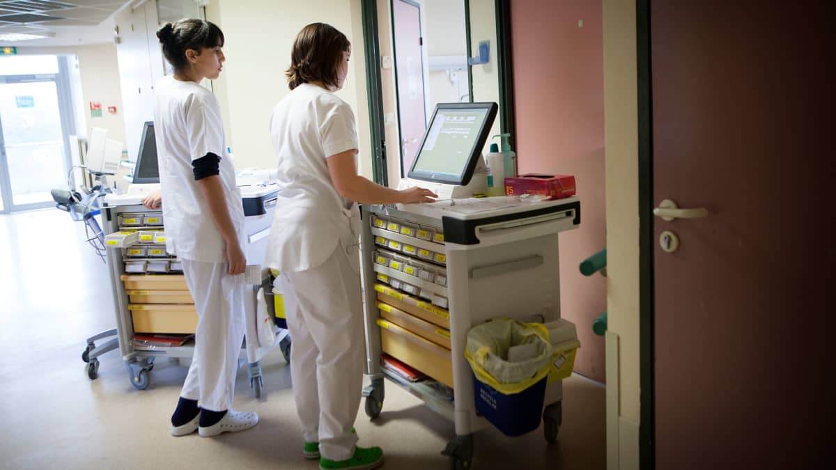 Två sjukskötare fotograferade bakifrån i en sjukhuskorridor.