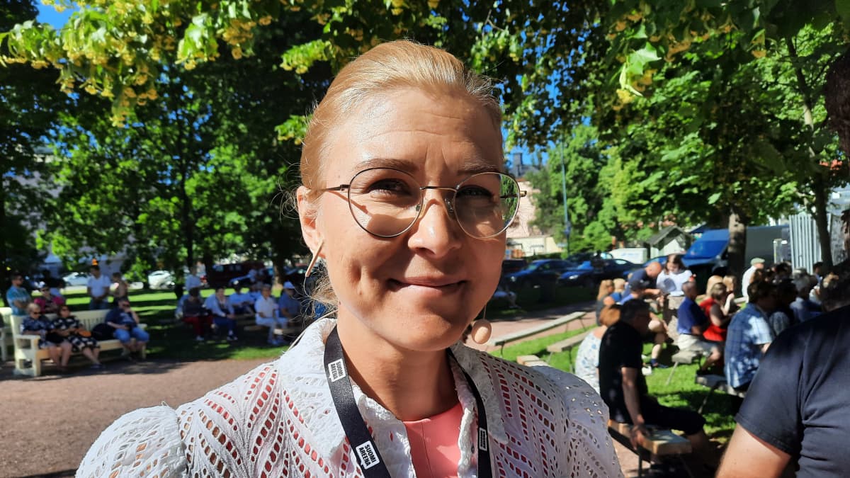 SDP:n kansanedustaja Niina Malm seisoo ulkona auringonpaisteessa, taustalla näkyy puita ja ihmisiä.