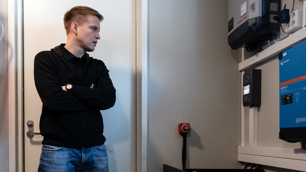 Jussi Tuunanen seisoo aurinkovoimalan akkujen vieressä varastotilassa.