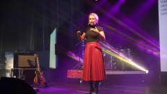 Punaiseen hameeseen ja mustaan t-paitaan pukeutunut Camilla Tuominen luennoi lavalla spottivalojen loisteessa.