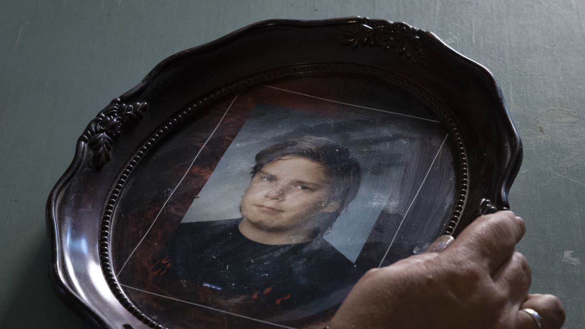 Hirvikolarissa kuolleen Toni Mannisen kuva kehyksissä. Hänen äitinsä käsi lepää valokuvan kehyksellä. 