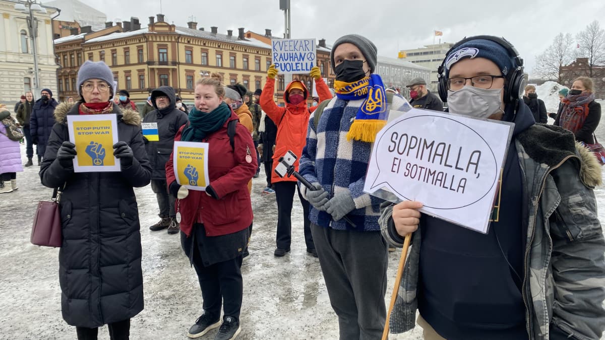 Mielenosoittajia Tampereen keskustorilla, Ukrainan rauhaa vaativassa mielenosoituksessa. Yhdellä mielenosoittajalla on kyltti, jossa lukee: "Sopimalla, ei sotimalla."