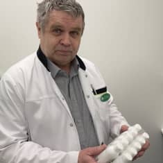 Valkotakkinen apteekkari pitelee käsissään pakkausta, jossa on kymmenen pientä muovipulloa.