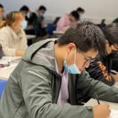 Aasialaistautaisia opiskelijoita luokkahuoneessa, katseet tableteissa.