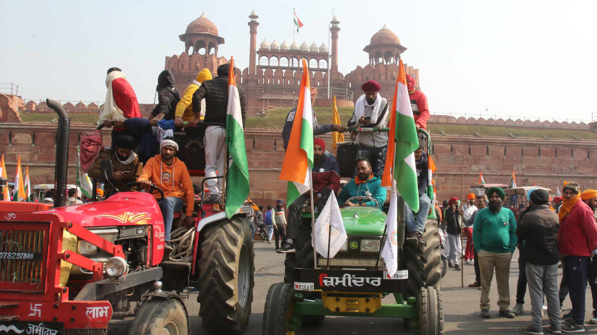 Kaksi trakotria on etualalla, punainen ja vihreä. Kuskin lisäksi molempien kyydissä on useita ihmisiä, ja traktorit on koristeltu Intian lipuilla. Taustalla näkyy Delhin Punainen linnoitus.