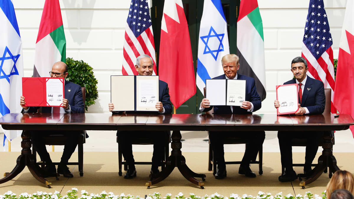 Vasemmalta Bahrainin ulkoministeri, Israelin pääministeri, Yhdysvaltain presidentti ja Arabiemiraattien ulkoministeri istuvat pöydän takana näyttäen yleisölle allekirjoitettuja sopimuksia, taustalla valtioiden lippuja