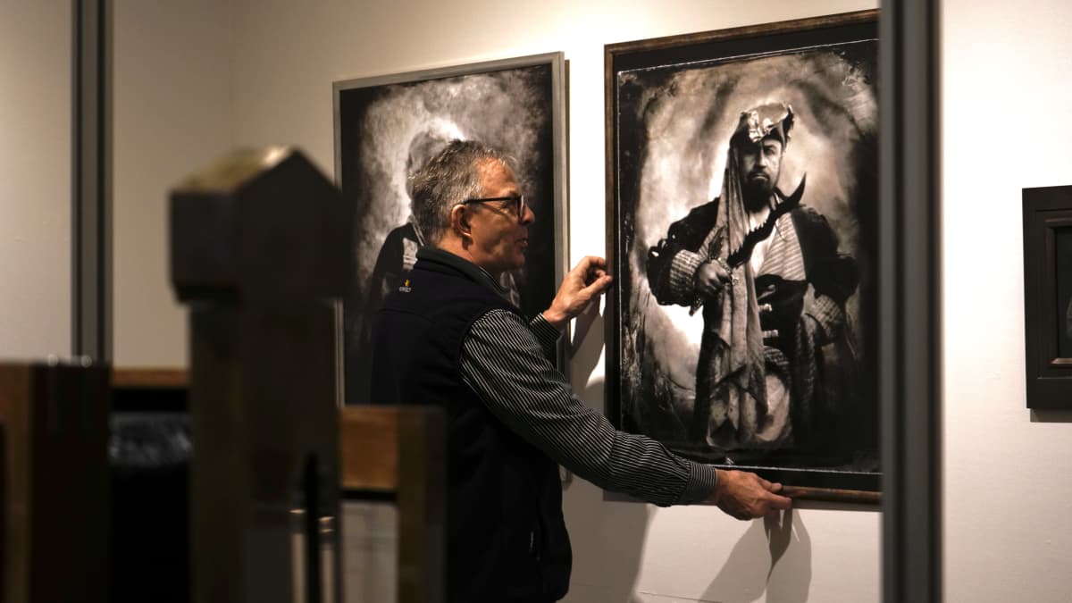 Pekka Homanen asettelee kehystettyjä kuvia esille Kainuun museolla.