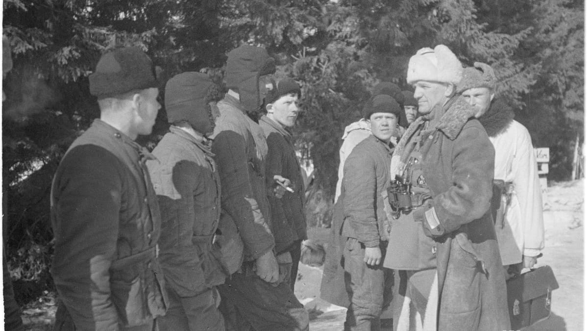 Venäläisiä sotilaita seisoo rivissä ja katsoo vakavin ilmein kernaalimajuri Pajaria, joka pitää käsiä taskussaan ja katsoo yhtä venäläisistä.
