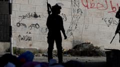 Aseistettu Israelin turvallisuusjoukkojen jäsen seisoo kiviseinän edessä. Seinään on maalattu töhryjä.