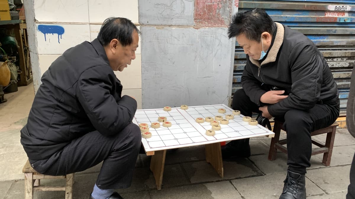 Kaksi miestä pelaa lautapeliä Wuhanissa kadulla.