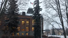Puiden takana punatiilinen Joensuun kaupungintalo. Alkutalvi, hieman lunta maassa ja pilvinen taivas.