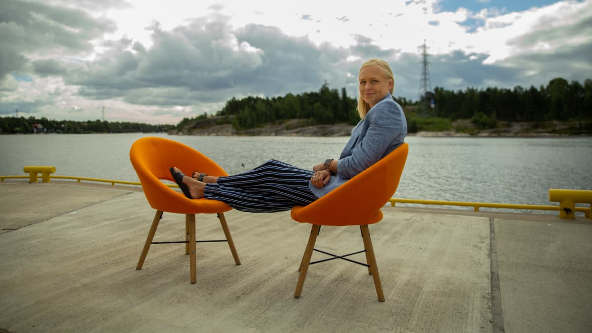 Elina Lepomäki istuu 8 minuuttia -ohjelman oranssilla tuolilla laiturilla Helsingin Kalasatamassa