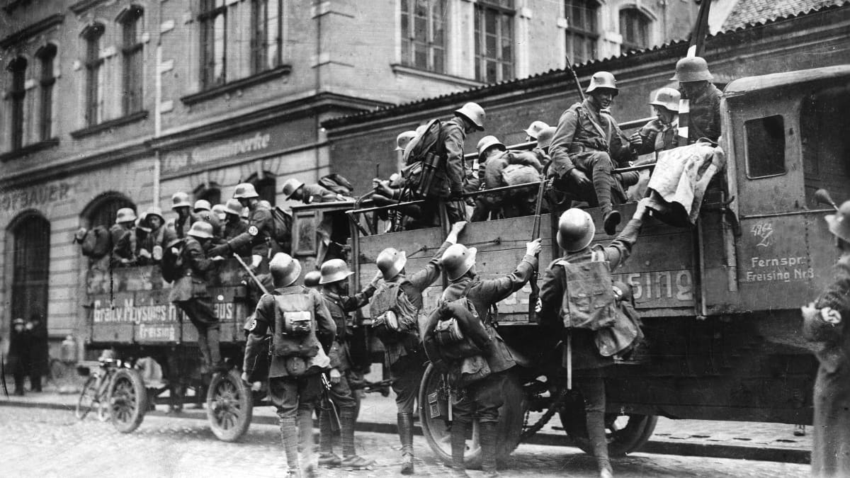 Saksalaisia sotilaita on nousemassa kuorma-autoihin. Heillä on sotilasvarusteet päällään, kypärät ja aseet sekä reput.