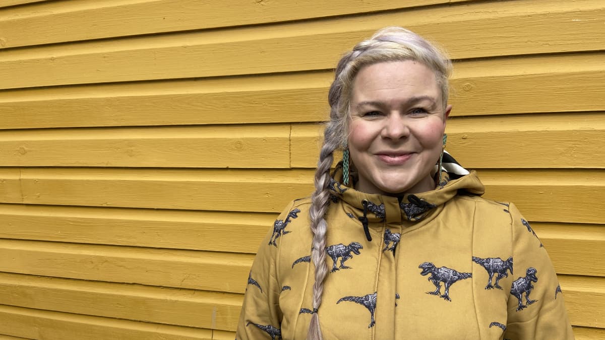 Suomen Harrastajateatteriliiton toiminnanjohtaja Sanna Saarela poseeraa keltaista talonseinää vasten