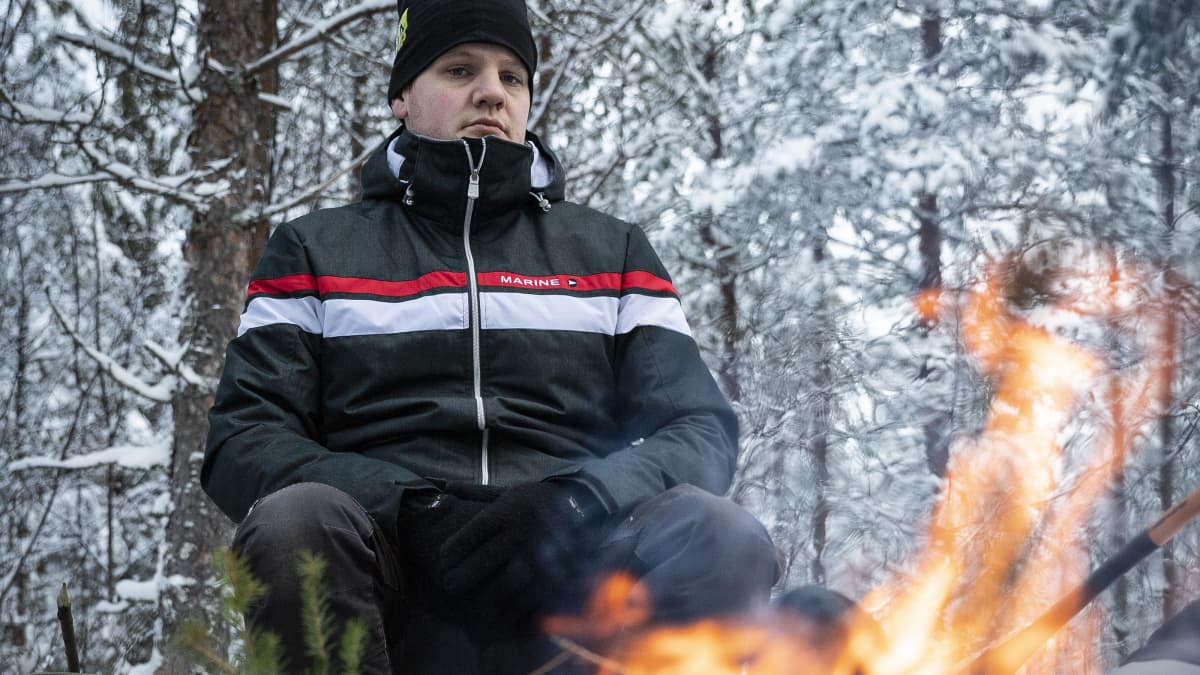 Mikko Karhukorpi istuu nuotion ääressä metsässä. 