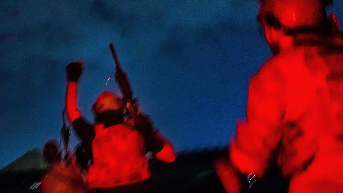 Sotilaita juoksee punaisessa valossa yöllä aseet ilmassa.