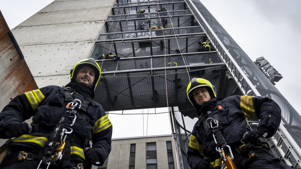 Kaksi pelastaja -opiskelijaa seisoo korkean tornin edustalla Kuopion Pelastusopistolla, jossa harjoittelevat laskeutumisesta köyden avulla korkealta.