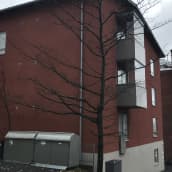 Punainen pienkerrostaloa Tampereen Armonkalliolla. Talon takana näkyy vanhempi punatiilinen kerrostalo ja Näsijärveä.