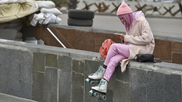 Nuori henkilö selailee puhelintaan Kiovan keskustassa rullaluistimet jalassa, taustalla tiesulku.