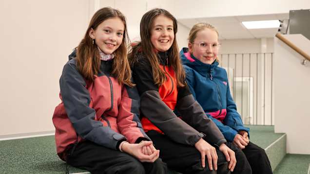 Tre personer sitter bredvid varandra på en grön trappa inomhus.