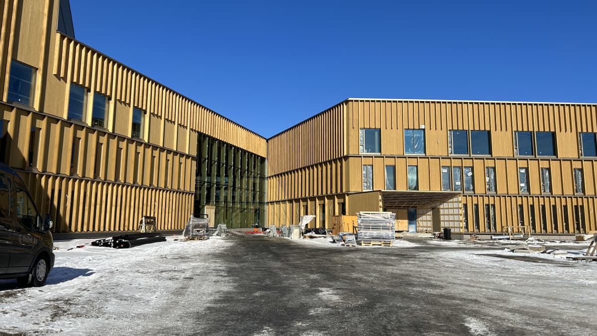Isossa rakennuksessa on puinen, rimoitettu julkisivu. Pihassa on lunta ja rakennustarvikkeita.