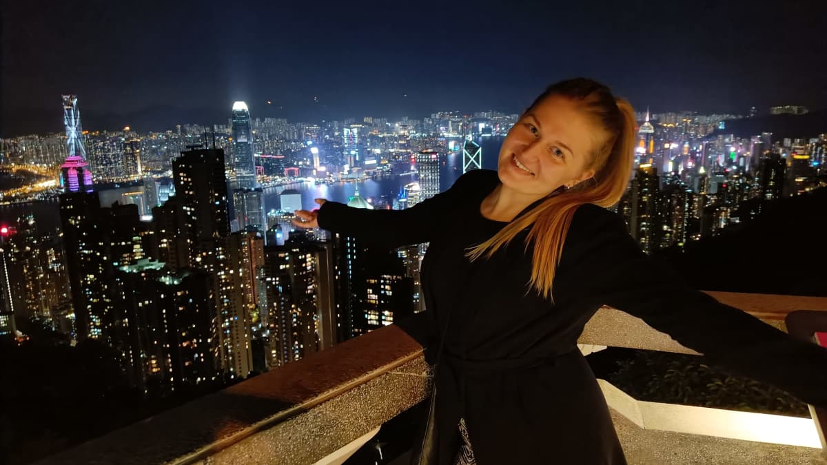 Nainen seisoo kädet avoinna. Taustalla öinen Hong Kong ja kaupungin valot.