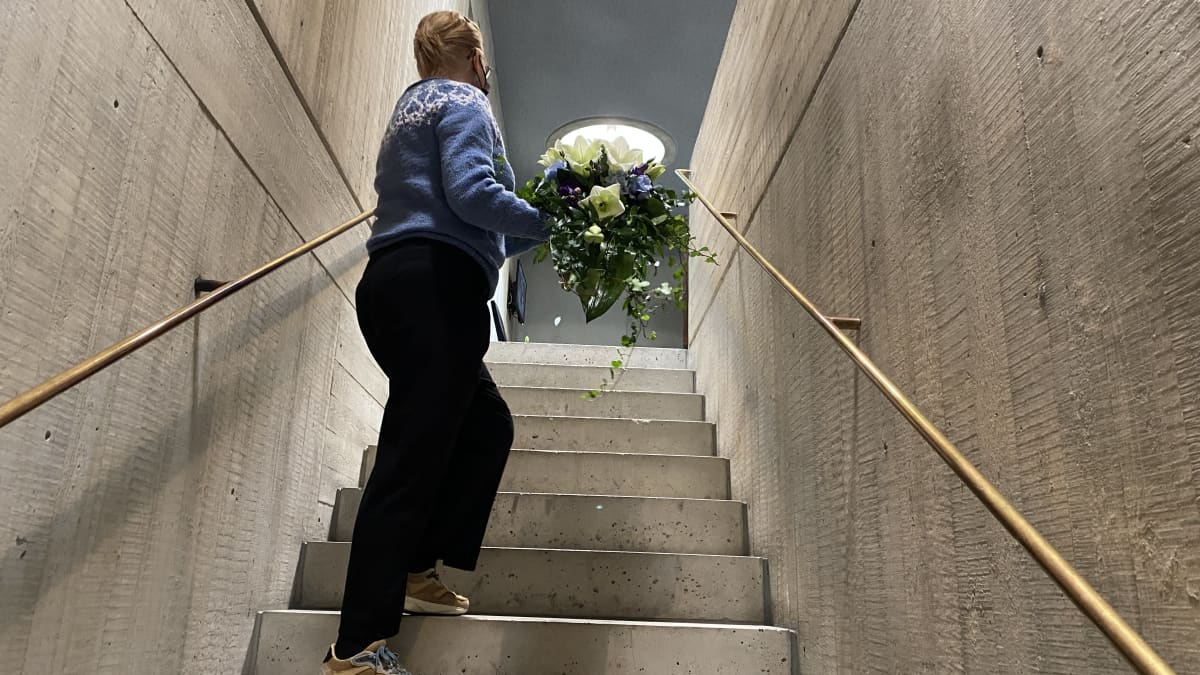Kukkakauppias vie hautajaiskukka-asetelmaa kappelin portaita pitkin