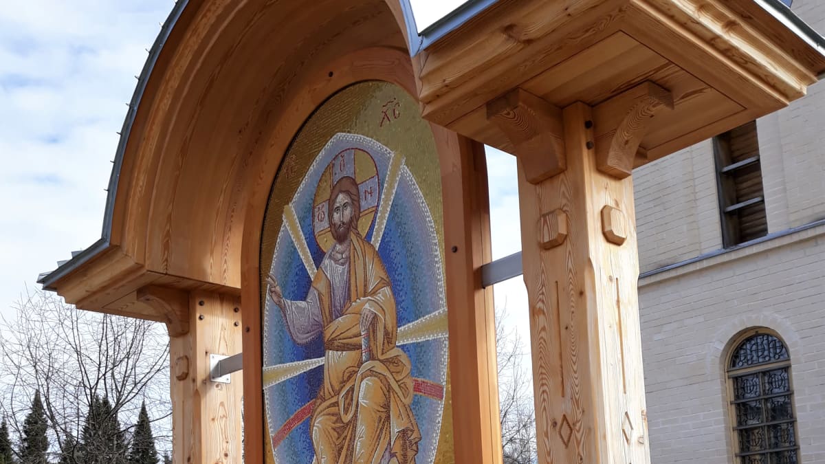 Mosaiikki-ikoni seisoo Puuartistin tekemän puisen holvikaarikatoksen suojissa ortodoksisen seminaarin edessä.