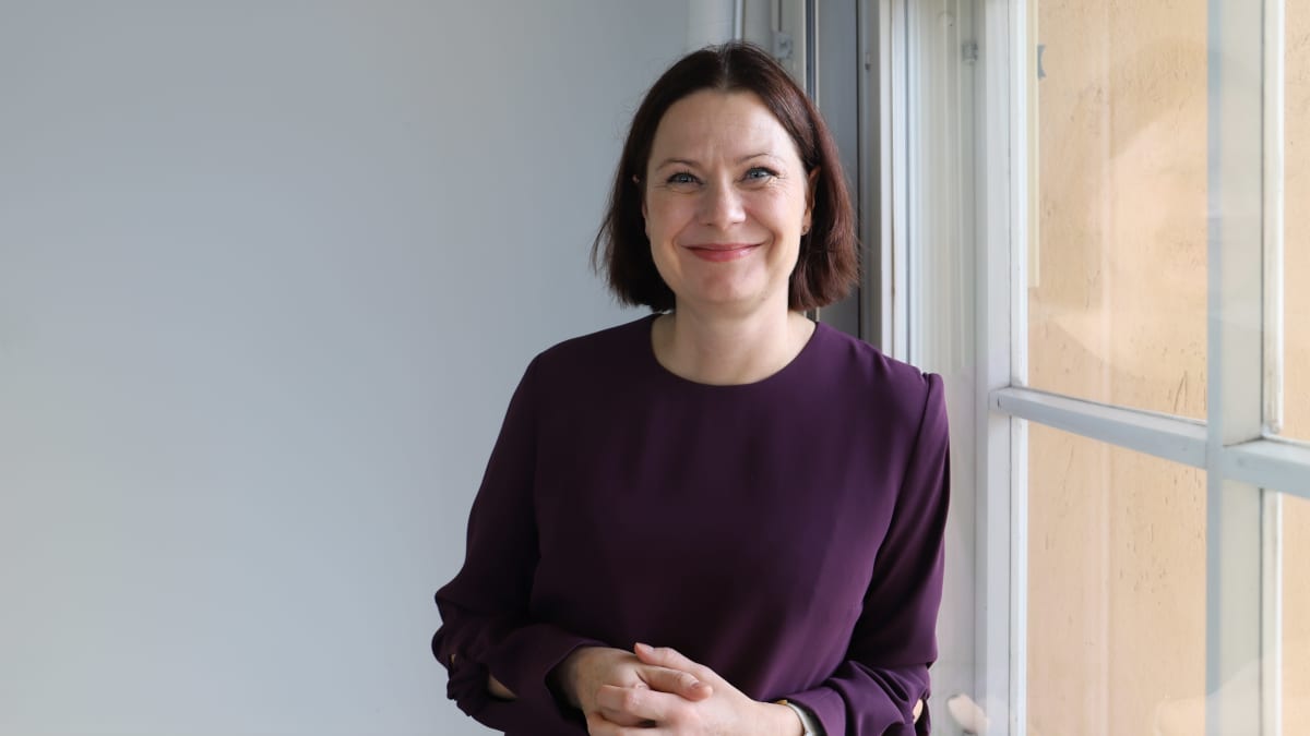 Minna Arve vid ett fönster. Hon ser rakt i kameran.