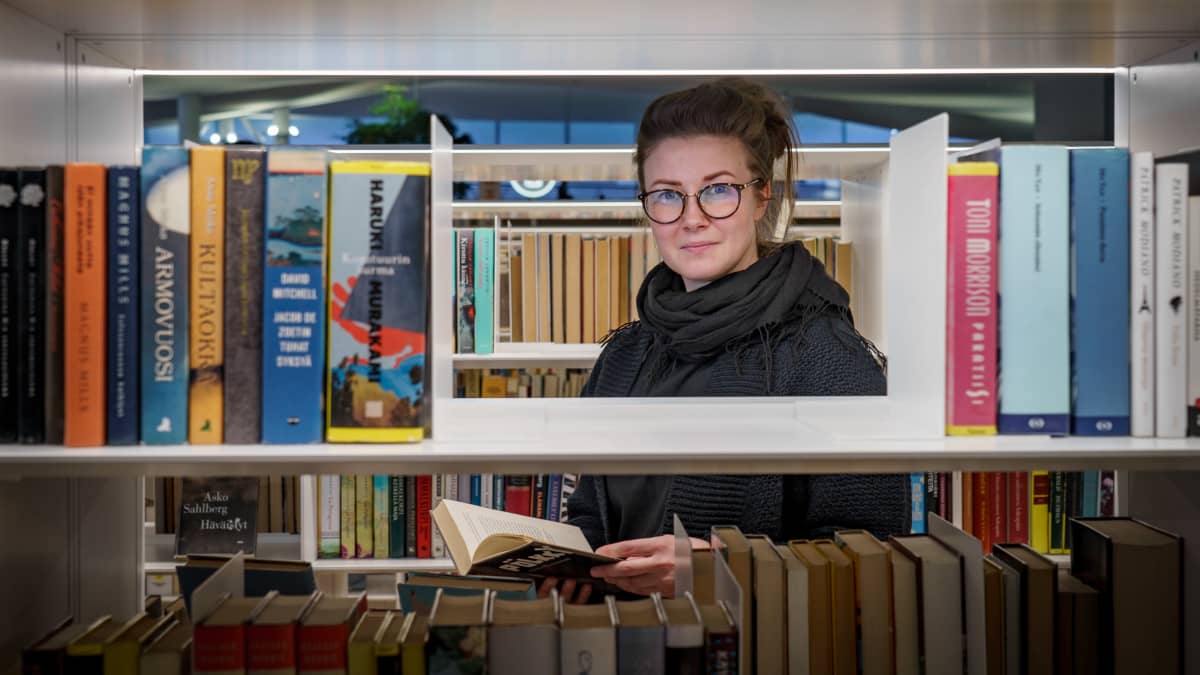 Kääntäjä Riina Behl katsoo kirjahyllyn läpi kohti kameraa.