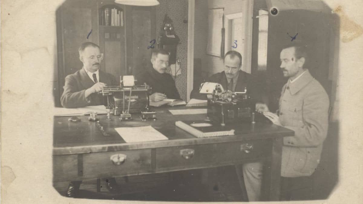 Vanhassa kuvassa neljä miestä toimistossa työskentelee kirjoituskoneilla. 
