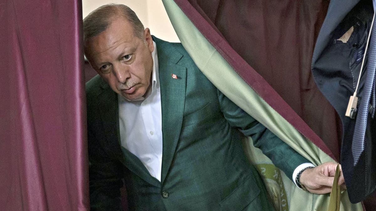 Poliitikko Recep Tayyip Erdogan astuu esiin viininpunaisen verhon takaa.