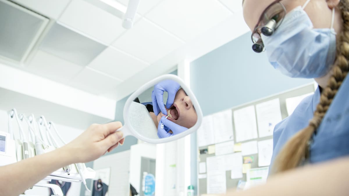 Hammaslääkäri näyttää potilaalle peilin kautta miten hampaiden välit tulisi puhdistaa.