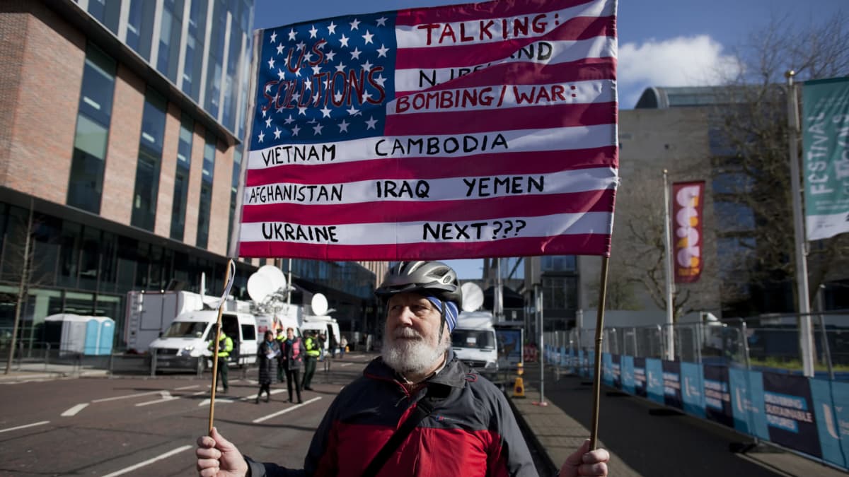 Mies kantaa Yhdysvaltojen lippua, johon on kirjoitettu maiden nimiä, joissa Yhdysvallat on käynyt sotia. 