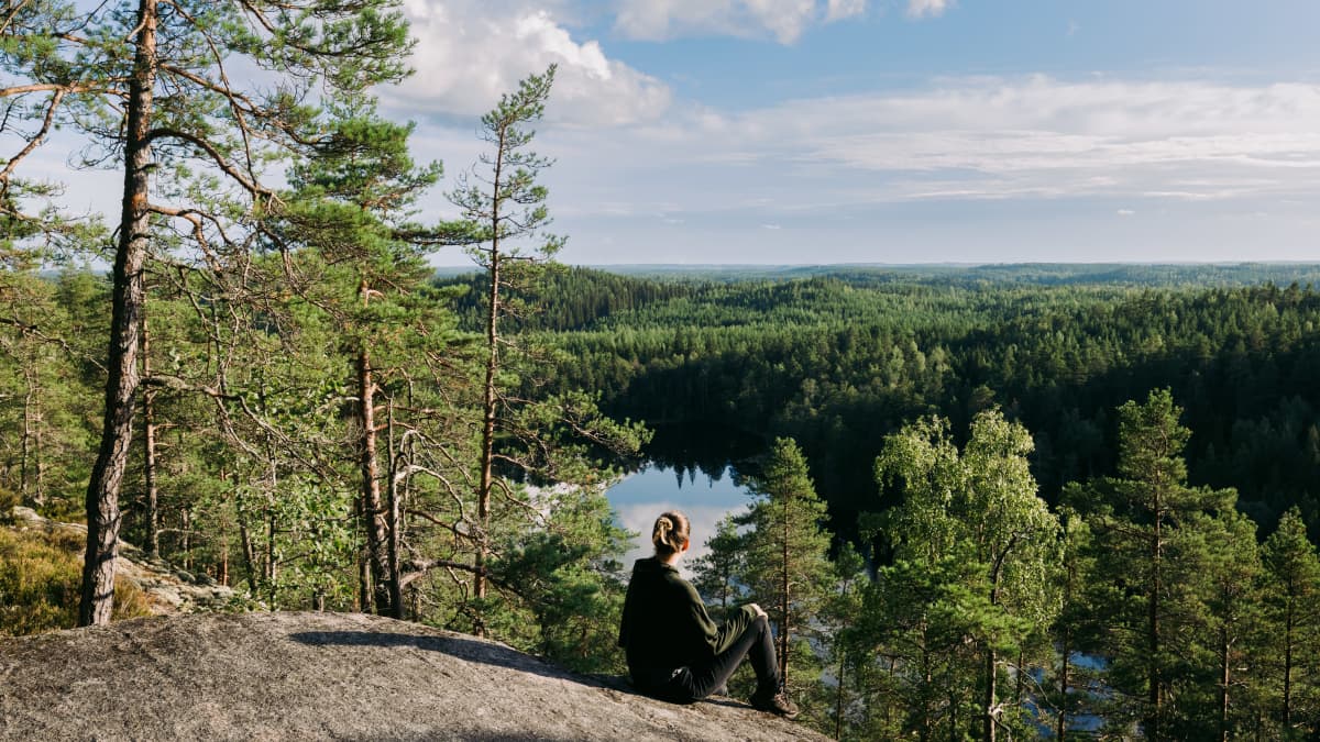 Nainen istuu kallioilla ja katsoo kohti järveä. 