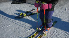 En utförsåkare står färdig med skidor och stavar påsatta.