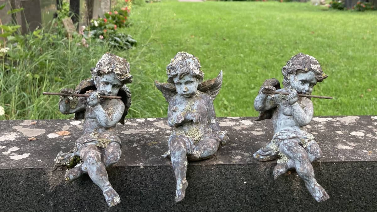 Kolme enkelifiguuria istuu hautakivellä