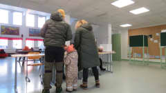 Tre personer, en man, en kvinna och ett barn med ryggen till. De ska rösta.