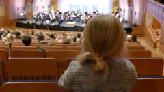 Tyttö kuuntelee orkesterimusiikkia Kuopion Musiikkikeskuksessa.