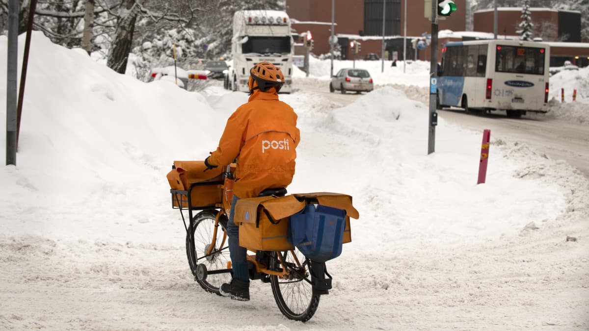 Postinjakaja pyöräilee talvisessa katumaisemassa.
