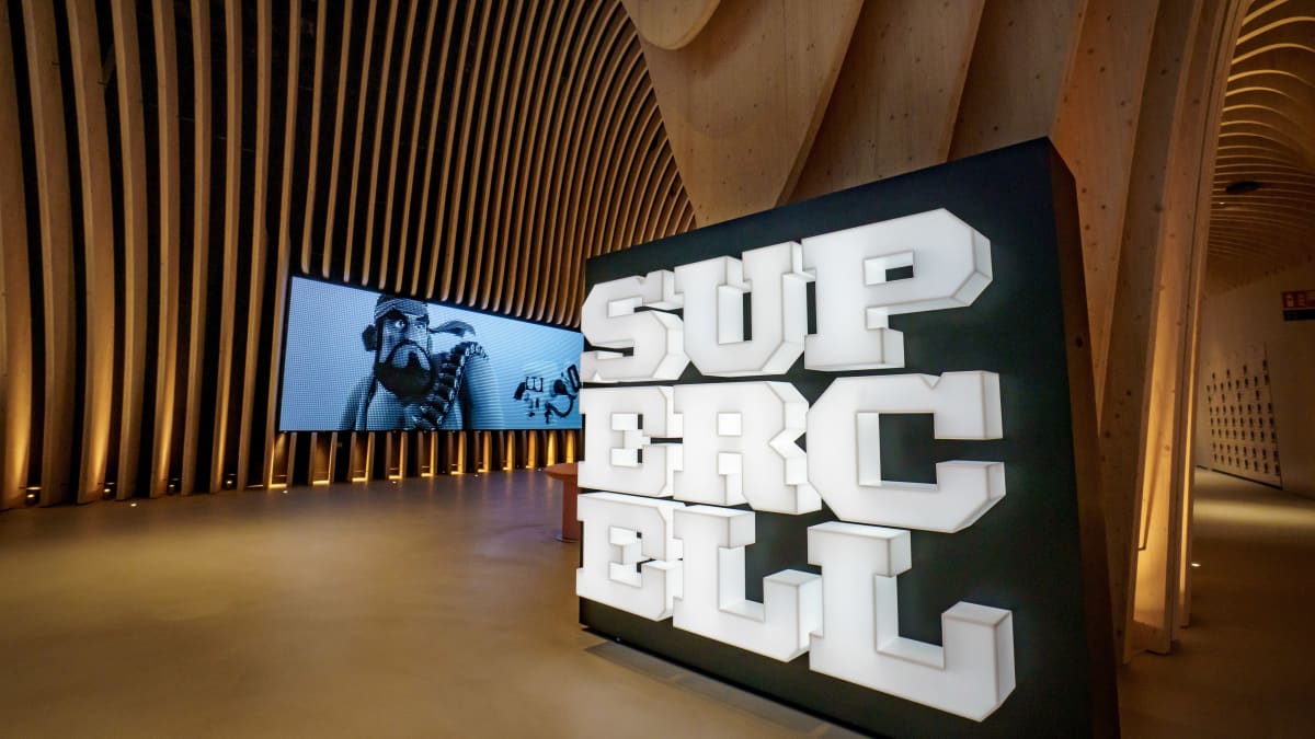 Supercellin pääkonttorin aula. Oikealla suuri Supercellin logo, taustalla isossa monitorissa pelihahmo.