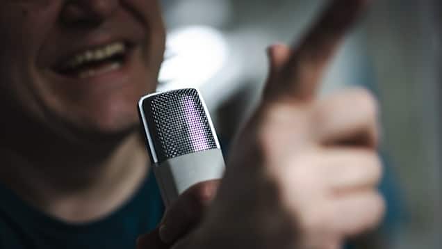 Närbild av en skrattande person som pratar i mikrofon.