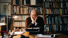Kirjailija Antti Tuuri istuu työhuoneellaan kirjoituskoneen äärellä ja nojaa käsiinsä.