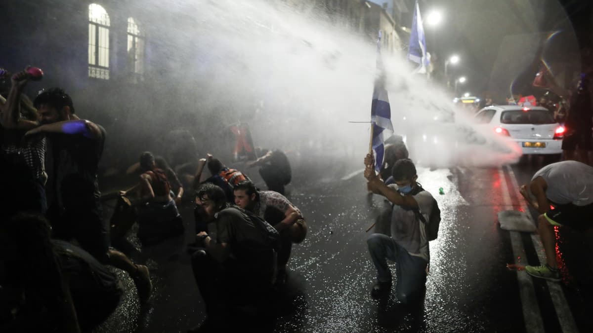 Poliisi ampuu vesitykillä mielenosoitukseen osallistuvia ihmisiä kadulla Israelissa.